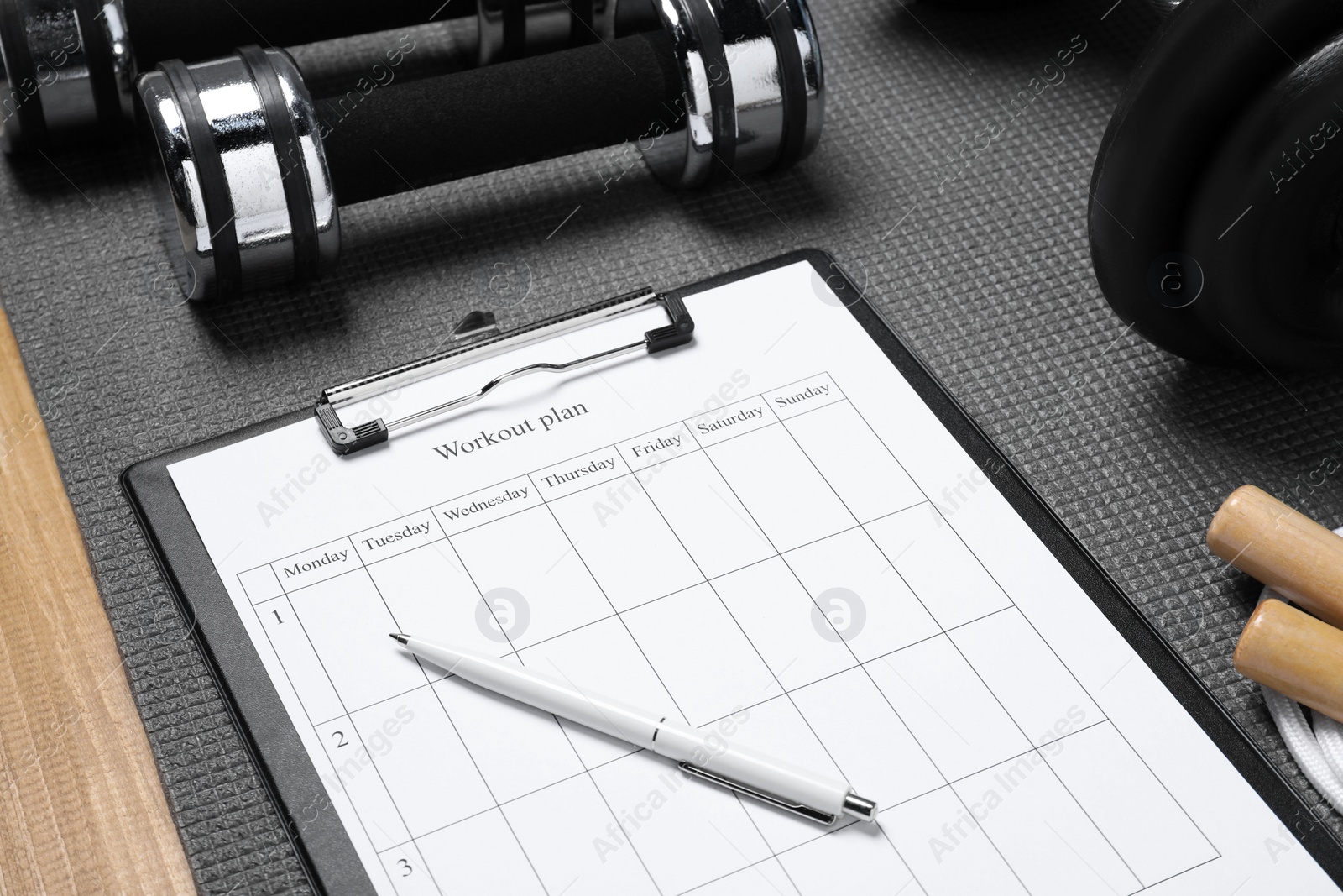 Photo of Clipboard with workout plan and sports equipment on wooden table, closeup. Personal training