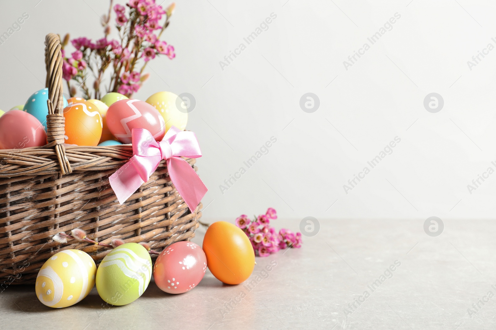 Photo of Wicker basket with painted Easter eggs and flowers on table, space for text