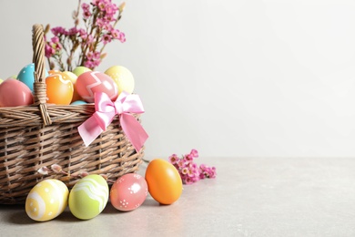 Photo of Wicker basket with painted Easter eggs and flowers on table, space for text