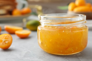 Delicious kumquat jam in jar on light grey marble table, closeup
