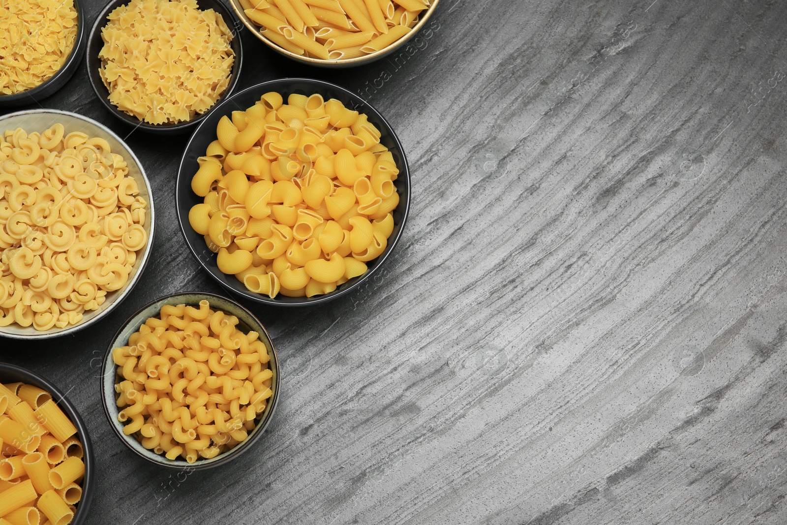 Photo of Different types of pasta on grey table, flat lay. Space for text