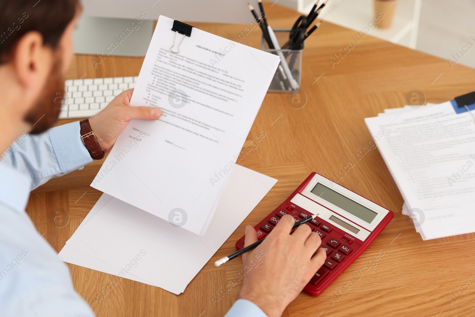 Photo of Man working with documents and using calculator at wooden table in office, above view