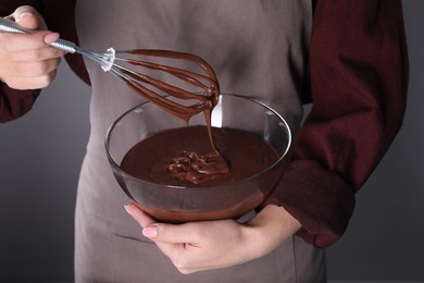 Photo of Woman with whisk making chocolate cream on grey background, closeup