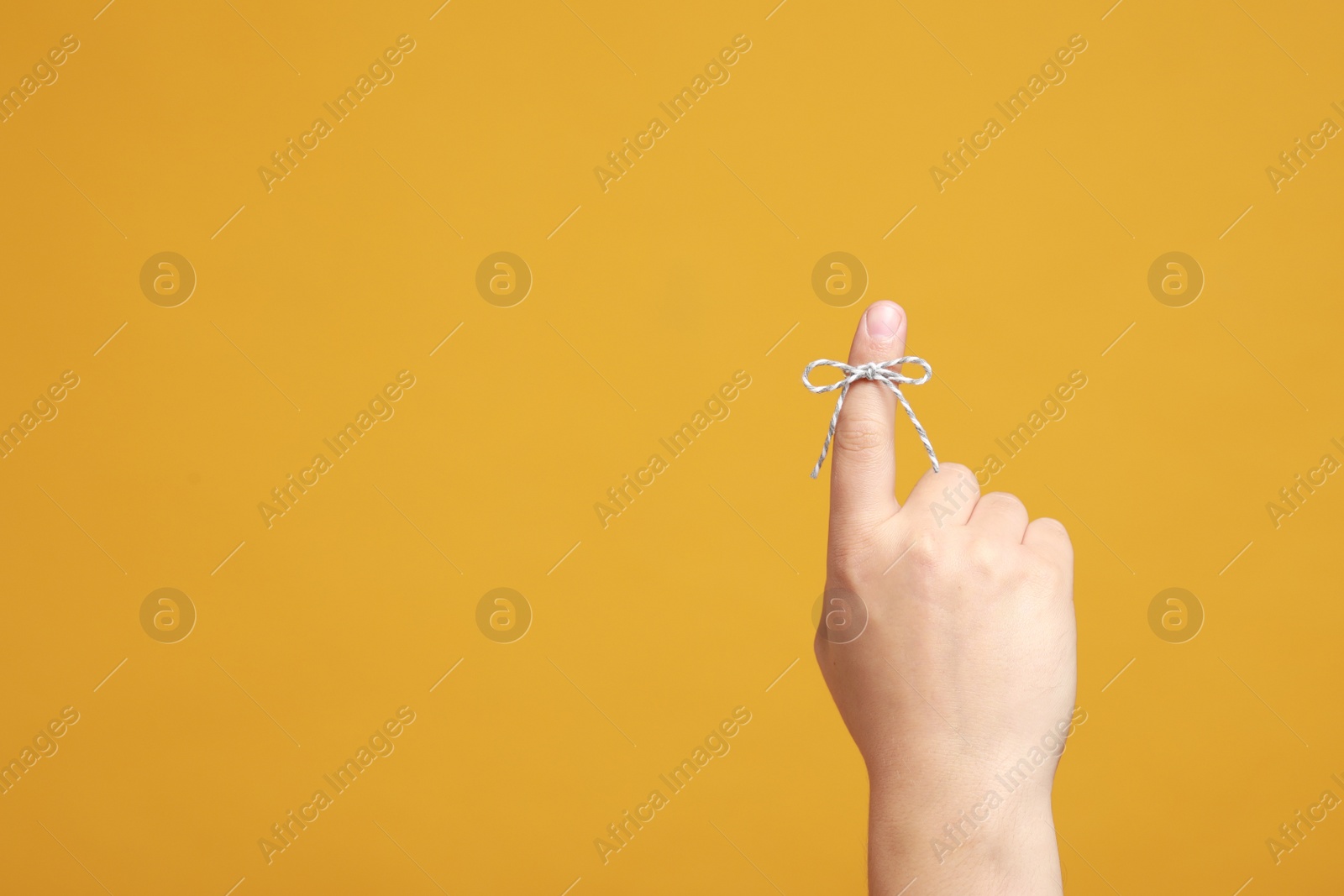 Photo of Man showing index finger with tied bow as reminder on orange background, closeup. Space for text