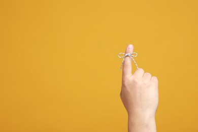 Man showing index finger with tied bow as reminder on orange background, closeup. Space for text