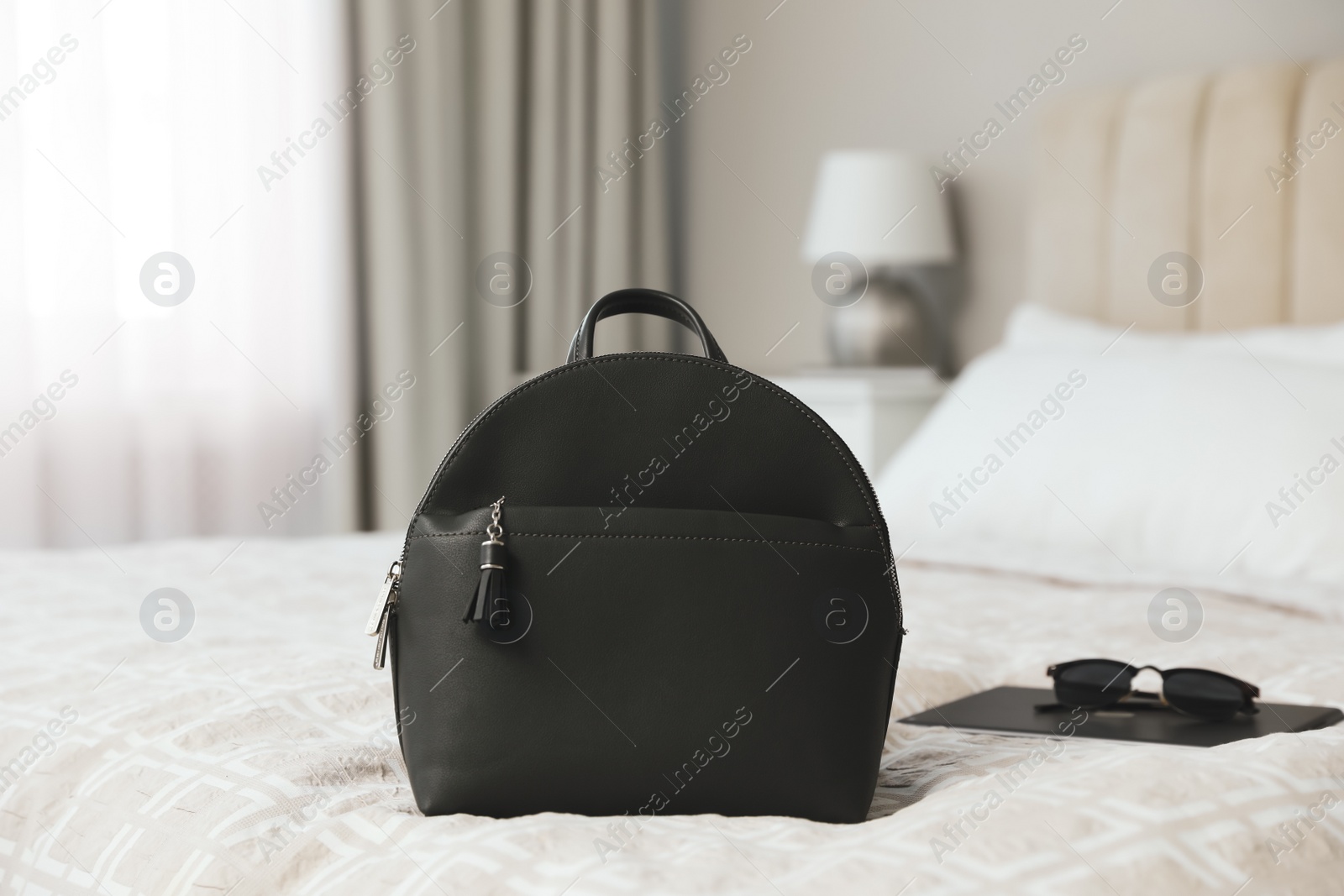 Photo of Stylish black backpack, tablet and sunglasses on bed in room