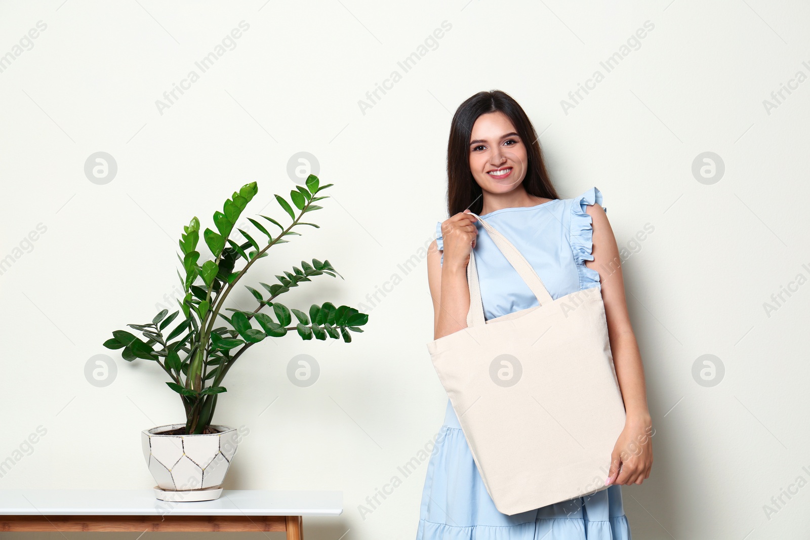 Photo of Beautiful young woman with stylish blank eco bag near white wall