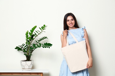 Beautiful young woman with stylish blank eco bag near white wall