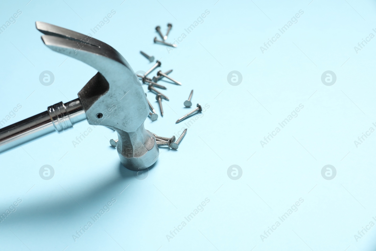 Photo of Hammer and metal nails on light blue background, closeup. Space for text