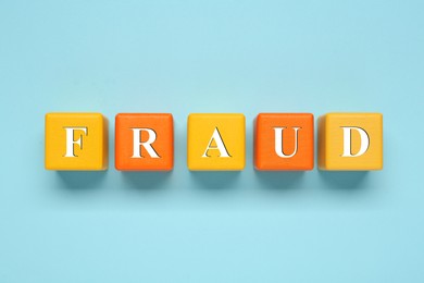 Word Fraud of wooden cubes with letters on light blue background, flat lay