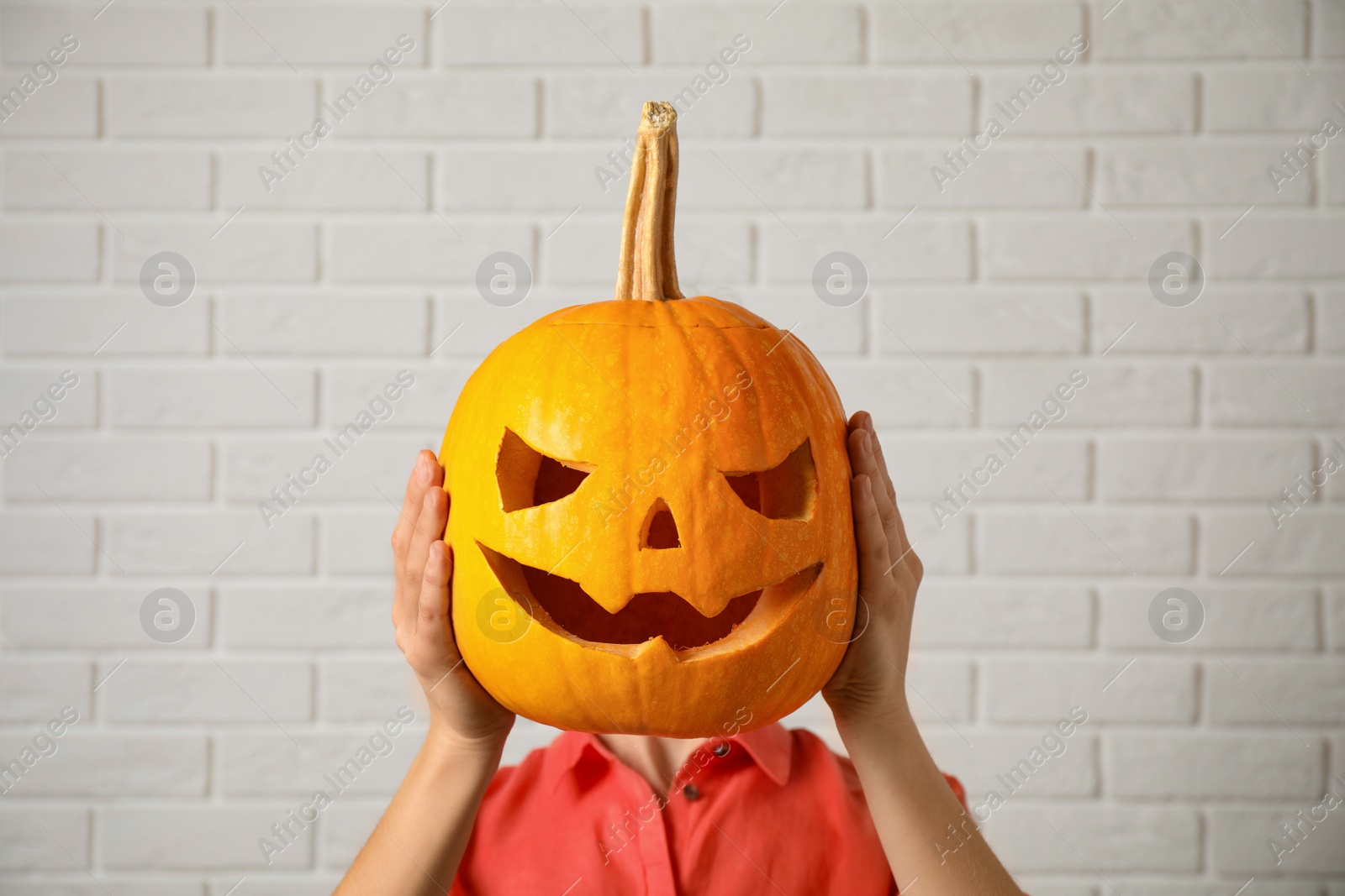 Photo of Woman with pumpkin head near white brick wall. Jack lantern - traditional Halloween decor