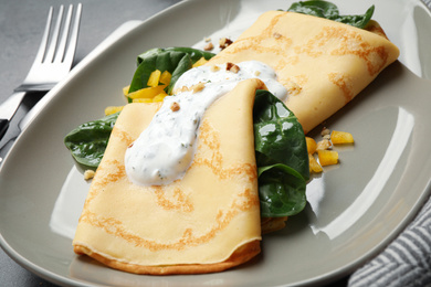 Delicious thin pancakes with spinach and sour cream on plate, closeup