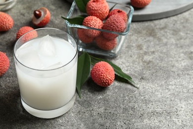Photo of Lychee juice and fresh fruits on grey table. Space for text