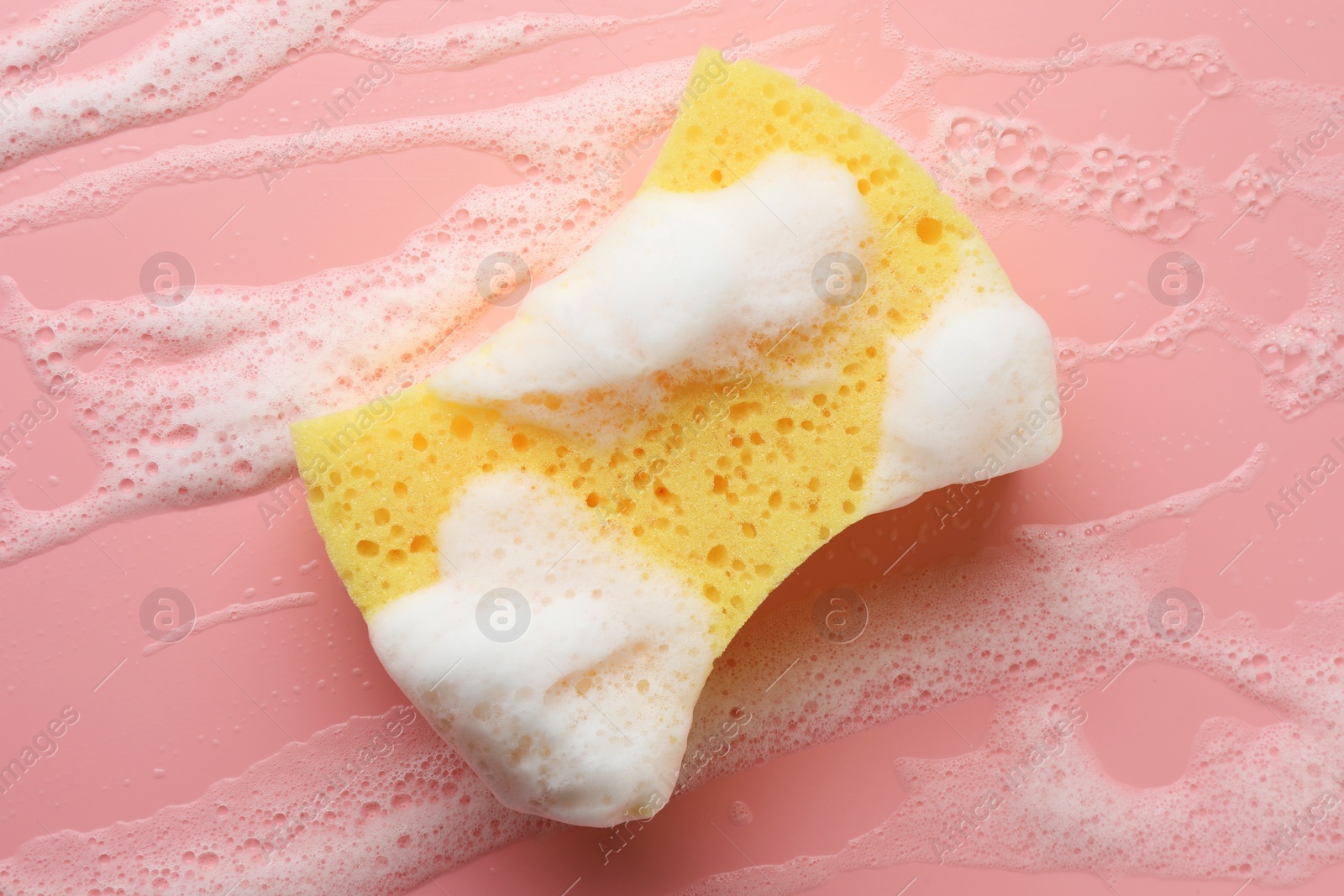 Photo of Yellow sponge with foam on pink background, top view