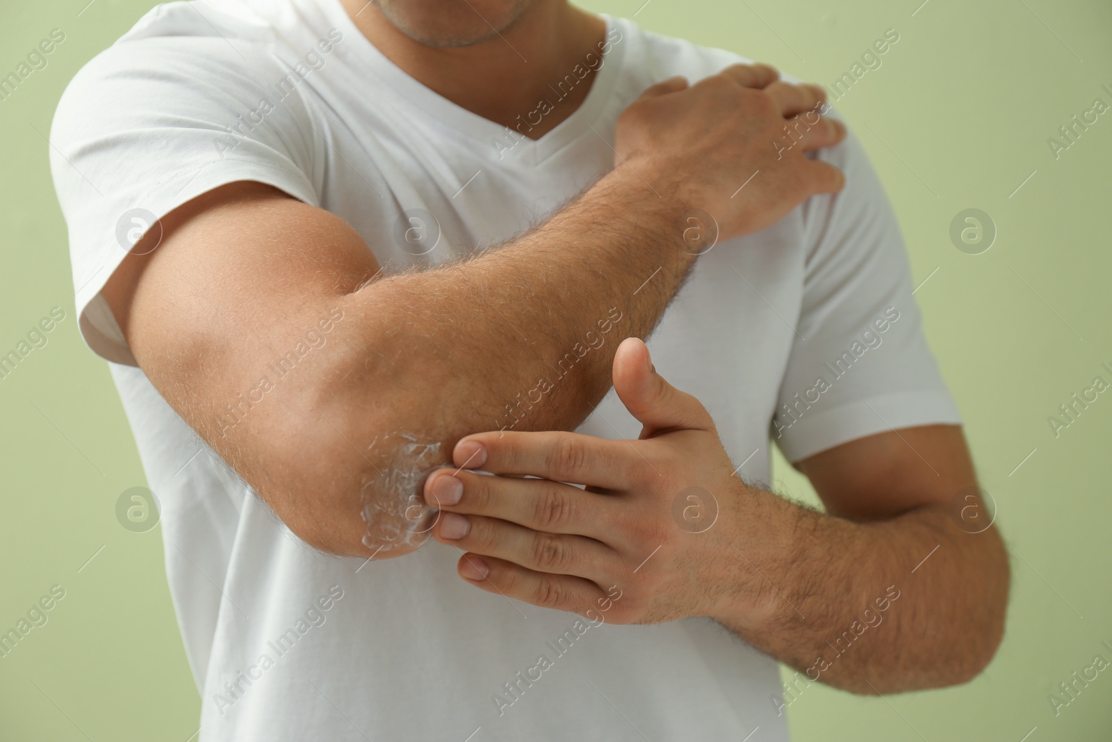 Photo of Man applying cream onto elbow on green background, closeup