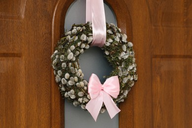 Wreath made of beautiful willow branches and pink bow on wooden door