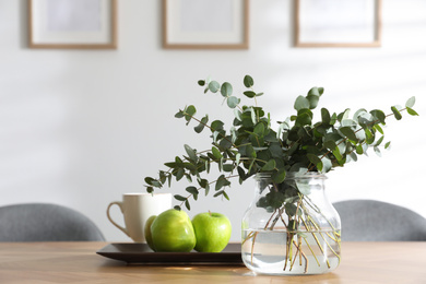Photo of Vase with beautiful bouquet, apples and cup of drink on wooden table indoors. Stylish interior design