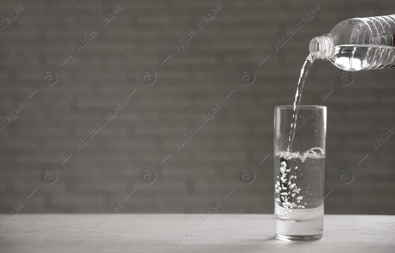 Photo of Pouring water from bottle into glass on table against blurred background. Space for text