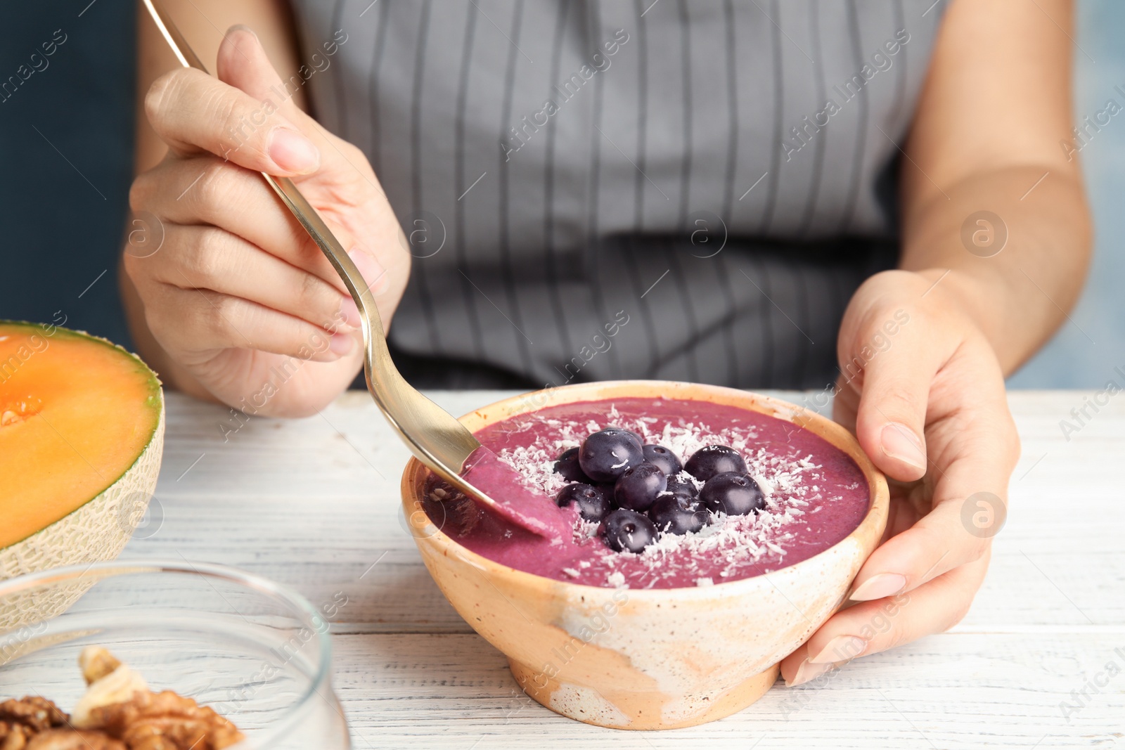 Photo of Woman eating tasty acai smoothie at table, closeup