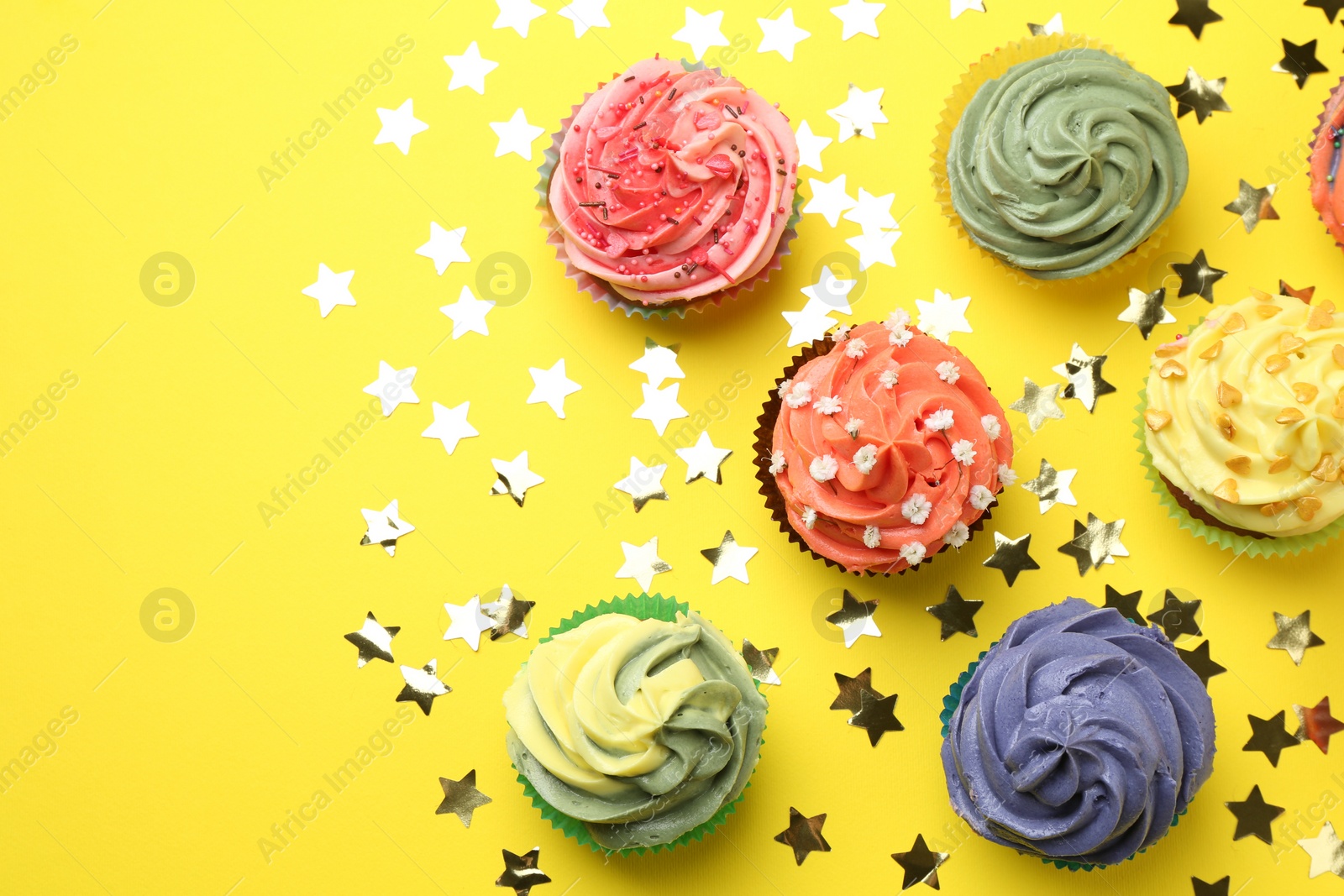 Photo of Delicious cupcake with bright cream and shiny confetti on yellow background, flat lay. Space for text