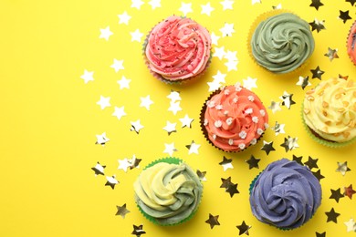 Photo of Delicious cupcake with bright cream and shiny confetti on yellow background, flat lay. Space for text