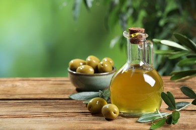 Photo of Jug of cooking oil, olives and green leaves on wooden table. Space for text