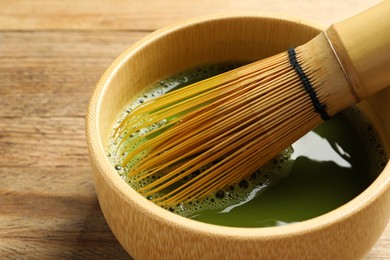 Photo of Cup of fresh matcha tea with bamboo whisk on wooden table, closeup