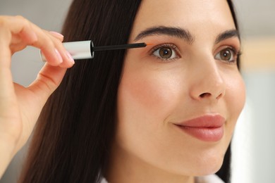 Photo of Beautiful woman applying serum onto her eyelashes indoors, closeup. Cosmetic product