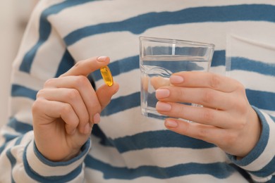 Woman holding glass of water and pill, closeup view