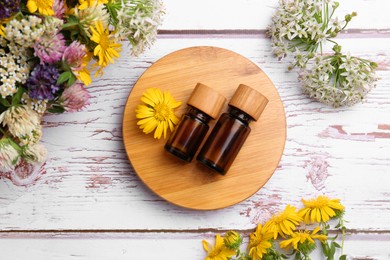 Photo of Bottles of essential oils and beautiful flowers on white wooden table, flat lay