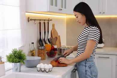Photo of Cooking process. Beautiful woman cutting tomato in kitchen