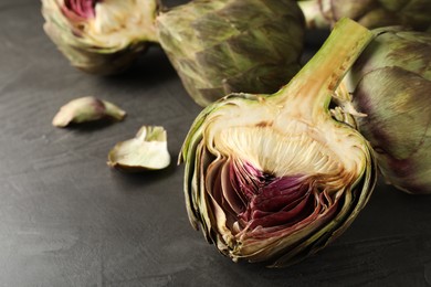 Photo of Cut and whole fresh raw artichokes on grey table, closeup. Space for text