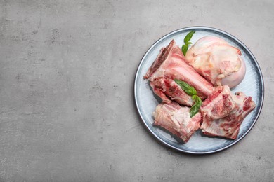 Photo of Plate with raw chopped meaty bones and basil on grey table, top view. Space for text