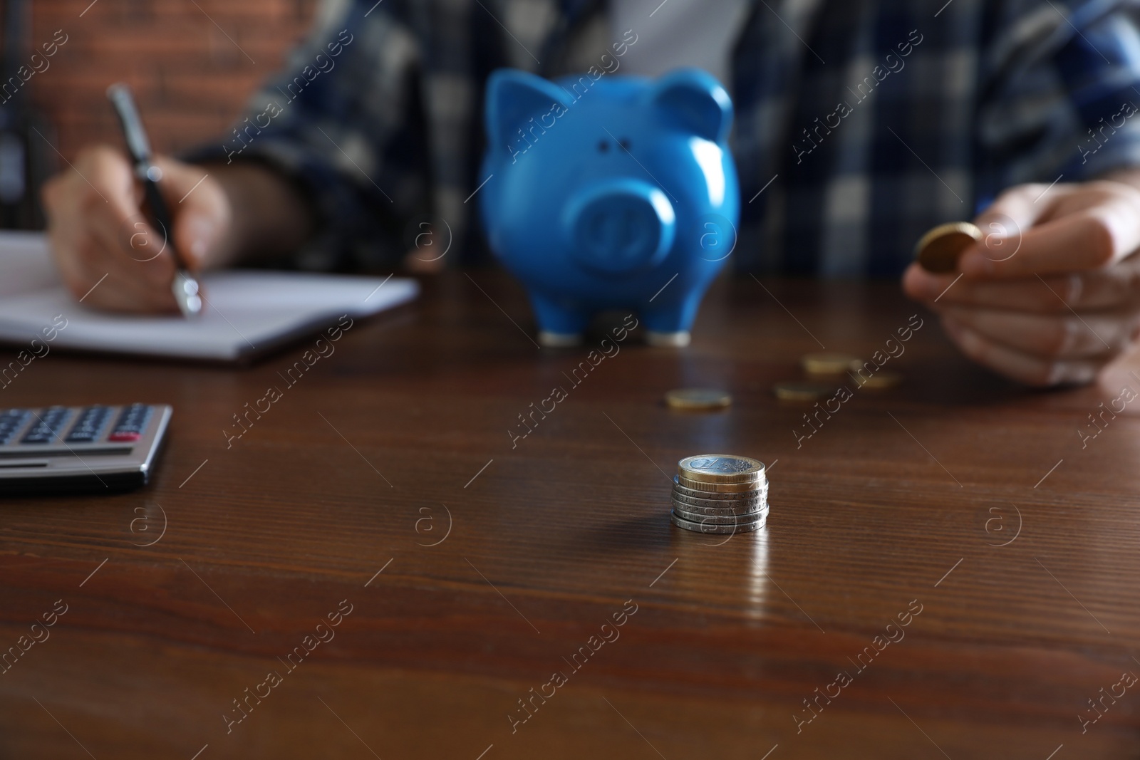 Photo of Man with piggy bank counting money at wooden table, focus on stack of coins
