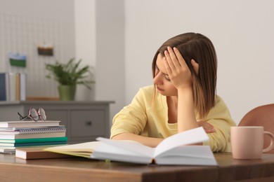 Photo of Young tired woman studying at wooden table in room