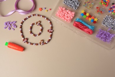 Photo of Handmade jewelry kit for kids. Colorful beads, necklace, bracelet and ribbon on beige background, flat lay. Space for text