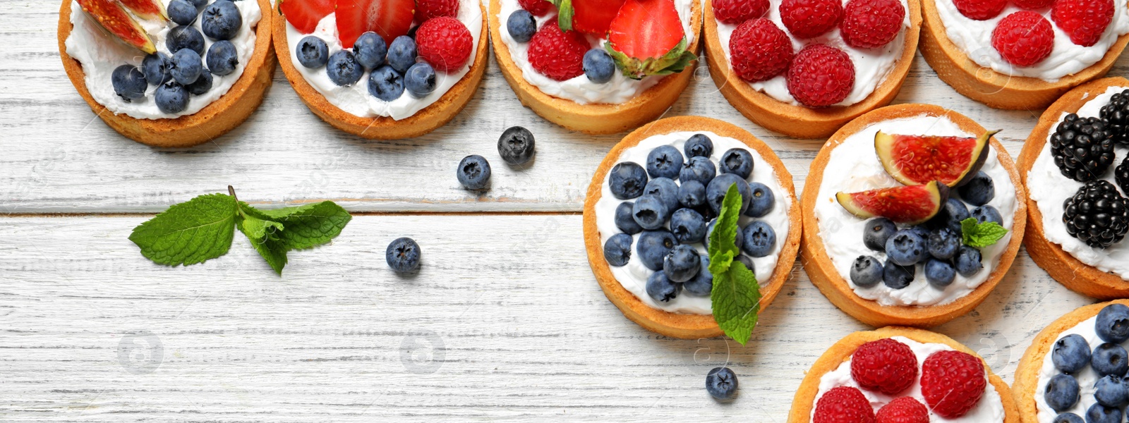 Image of Delicious tartlets with fresh berries on white wooden table, flat lay. Banner design