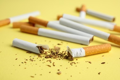 Photo of Broken and whole cigarettes on yellow background, closeup. Quitting smoking concept