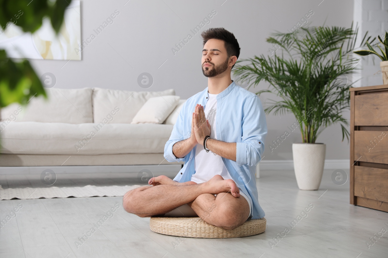 Photo of Young man meditating on straw cushion at home