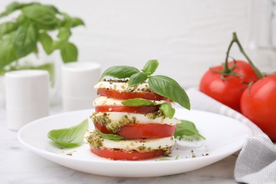 Plate of stacked Caprese salad with pesto sauce on white marble table, closeup