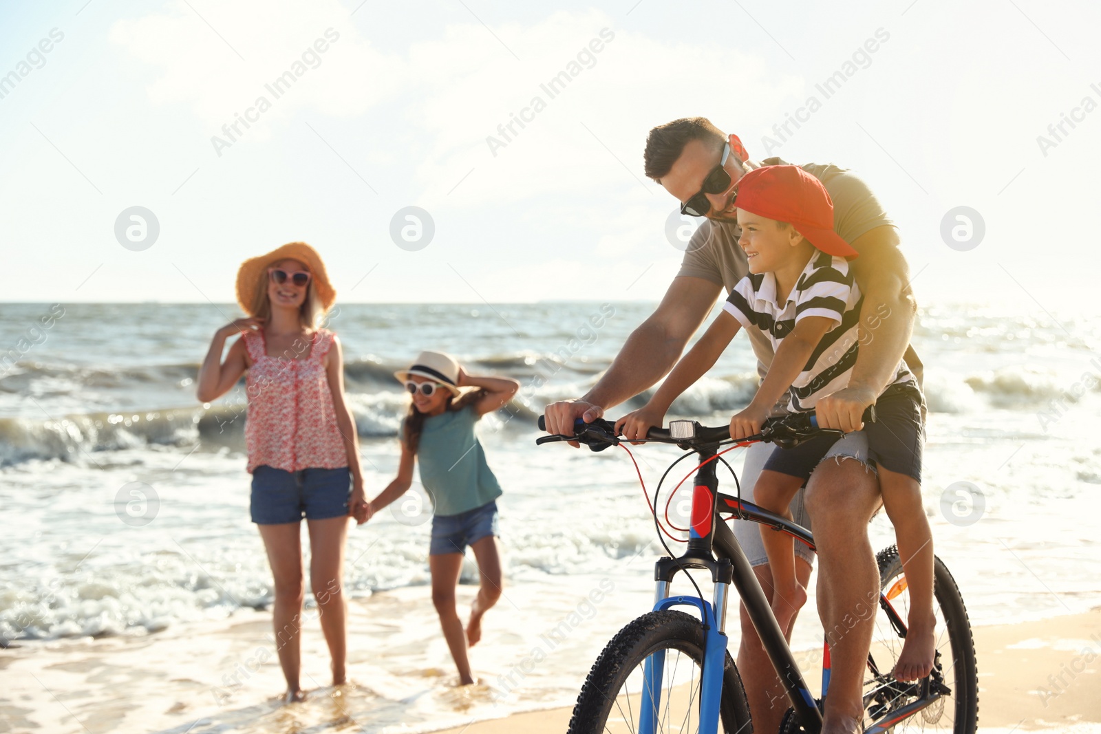 Photo of Happy family with bicycle on sandy beach near sea