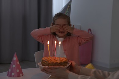 Photo of Birthday celebration. Mother holding tasty cake with burning candles near her daughter indoors