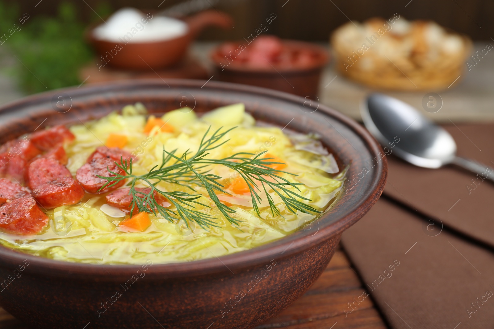 Photo of Bowl of delicious sauerkraut soup with smoked sausages and dill on table, closeup