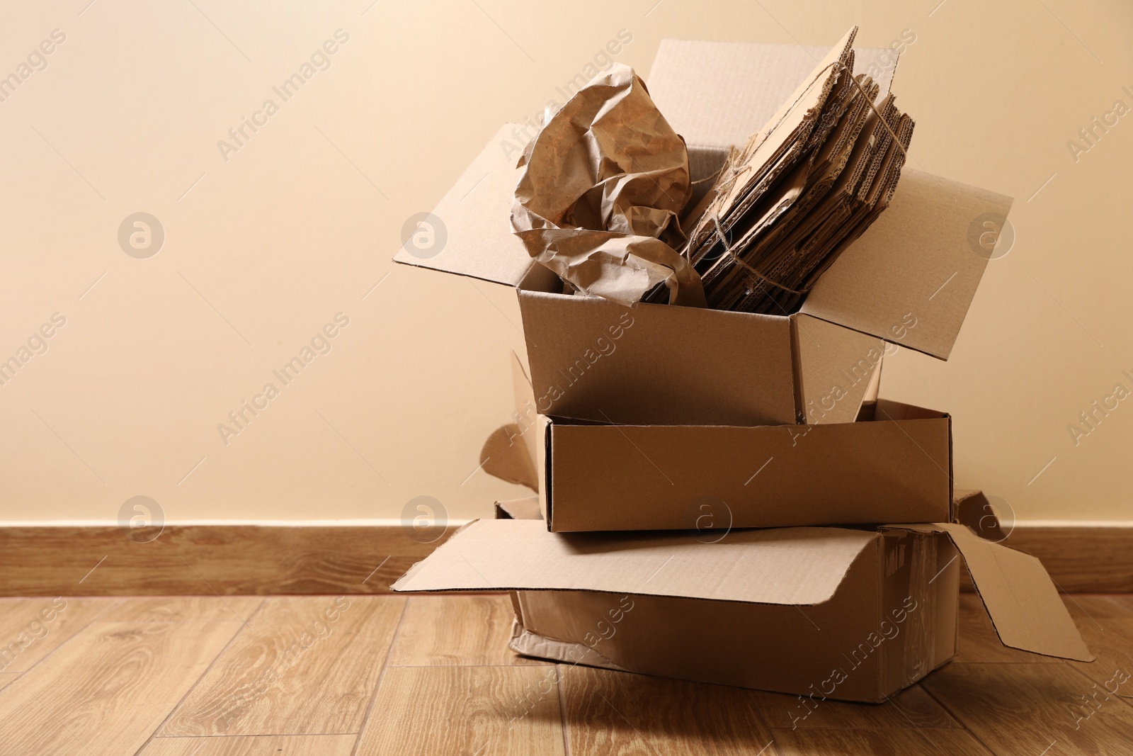 Photo of Heap of waste paper on wooden floor near beige wall, space for text