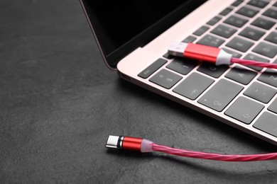 Photo of Red USB cable with type C connector and laptop on black slate table, closeup