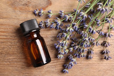 Bottle of essential oil and lavender flowers on wooden table, flat lay