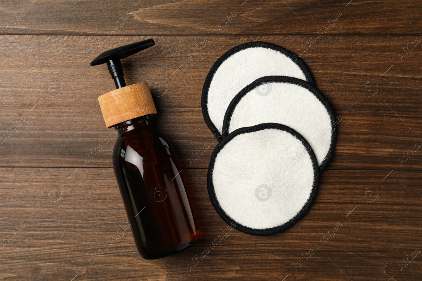 Photo of Soap dispenser and makeup remover pads on wooden background, flat lay. Conscious consumption