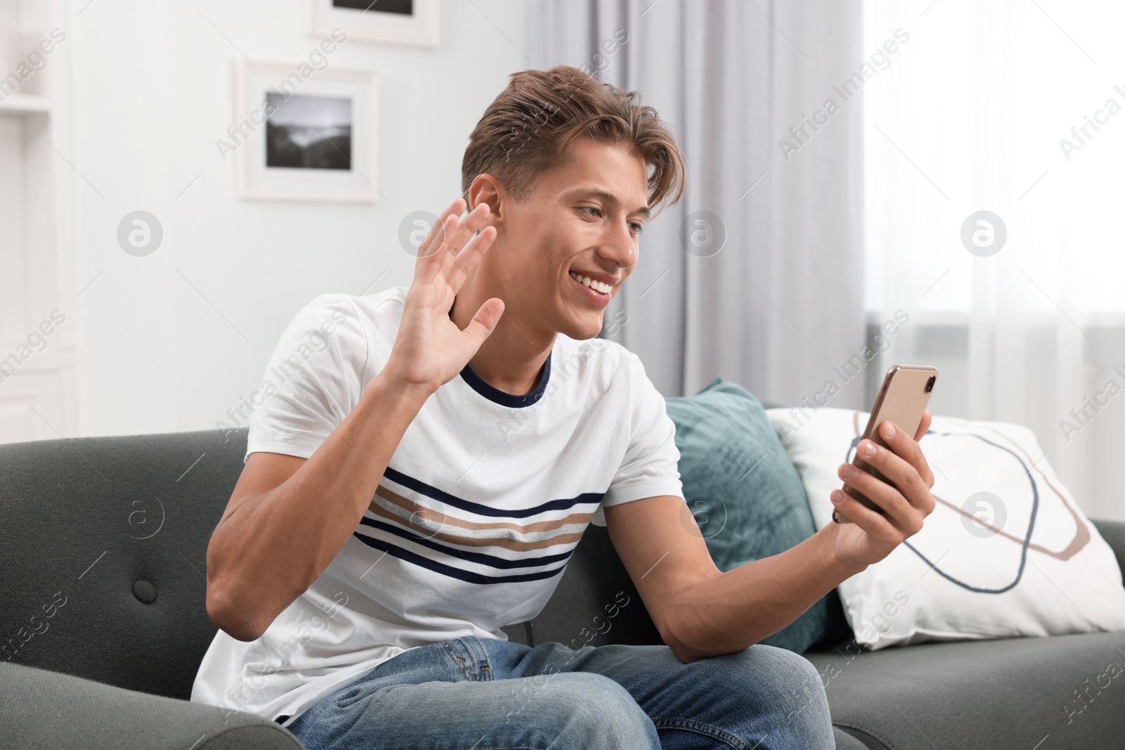 Photo of Happy young man having video chat via smartphone on sofa indoors