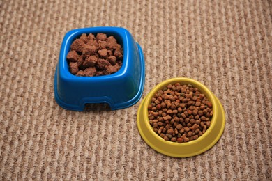 Dry and wet pet food in feeding bowls on soft carpet, above view