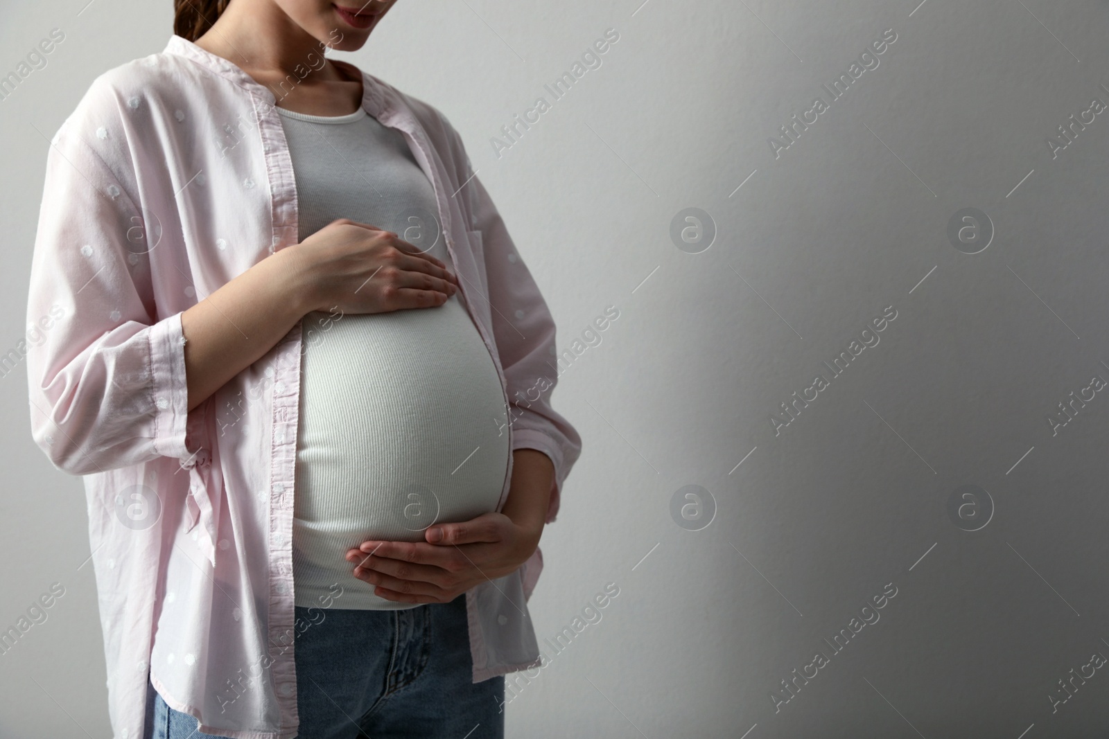 Photo of Young pregnant woman on light grey background, closeup. Space for text